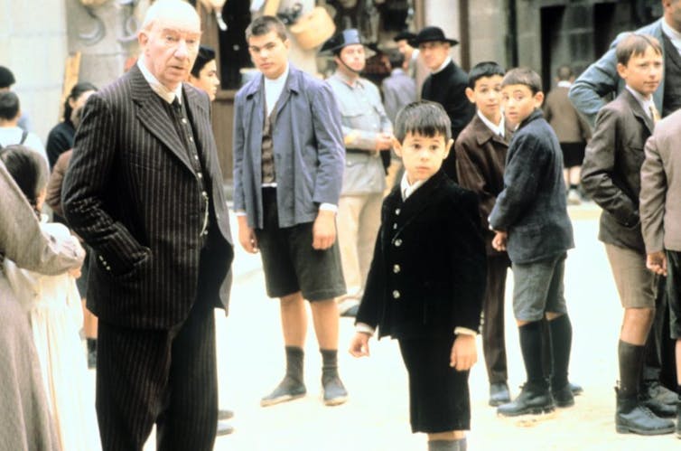 Un hombre mayor vestido con traje mira fuera de campo al lado de un niño también vestido de traje.