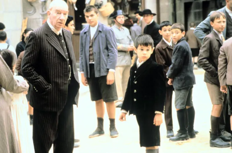 Un hombre mayor vestido con traje mira fuera de campo al lado de un niño también vestido de traje.