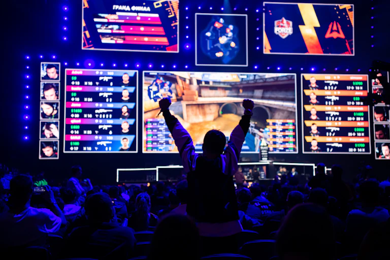 eSports gaming event. Big illuminated main stage and screen and a fan with a hands raised at arena.