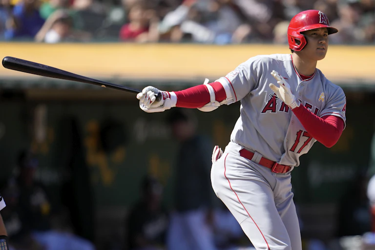 An Asian man in a grey and red baseball uniform swings a bat