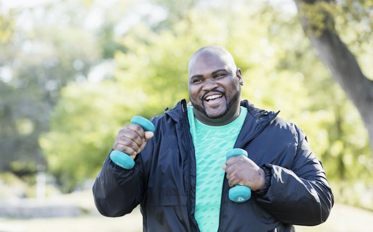 smiling man outside in jacket with small hand weights