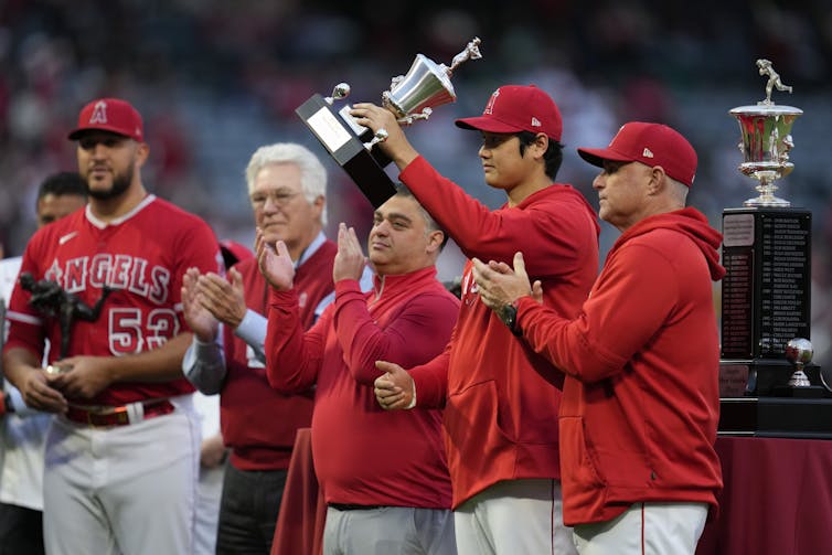 A group of men in red sweaters surround an Asian man who is holding a trophy