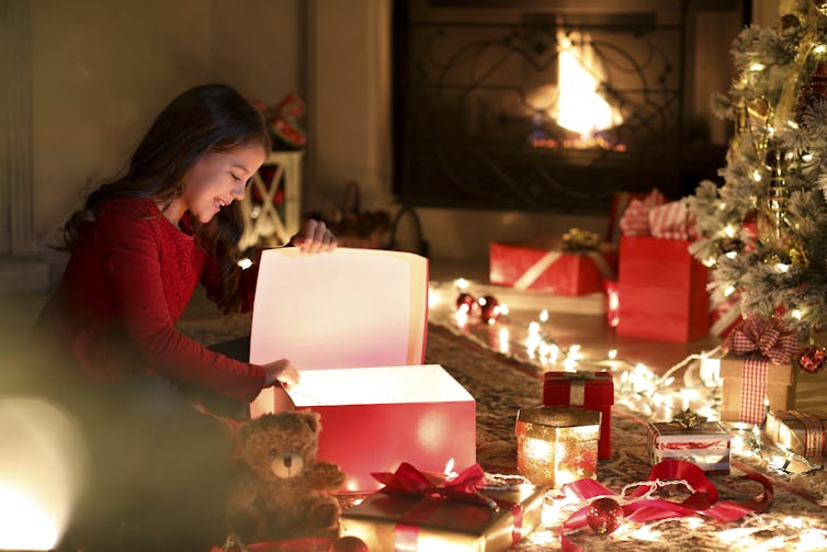 χαρούμενο κορίτσι ανοίγει ένα κουτί που λάμπει από μέσα από ένα χριστουγεννιάτικο δέντρο
