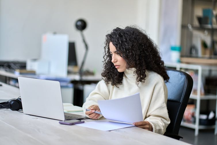 A woman checks a computer and a piece of paper closely.