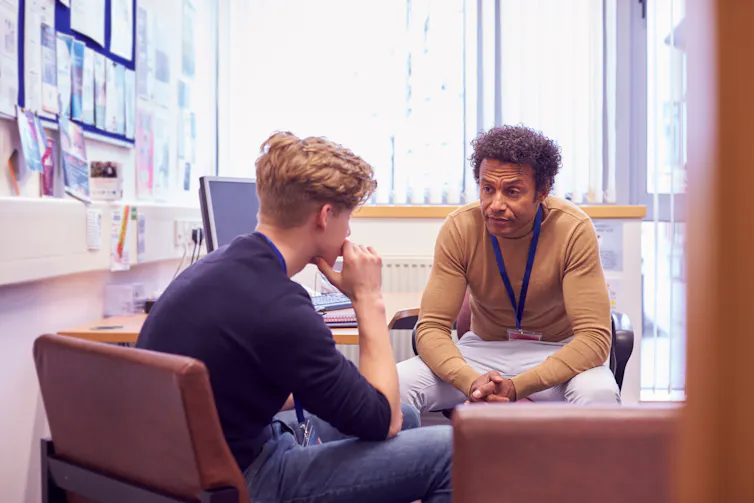 man speaks with younger man in office
