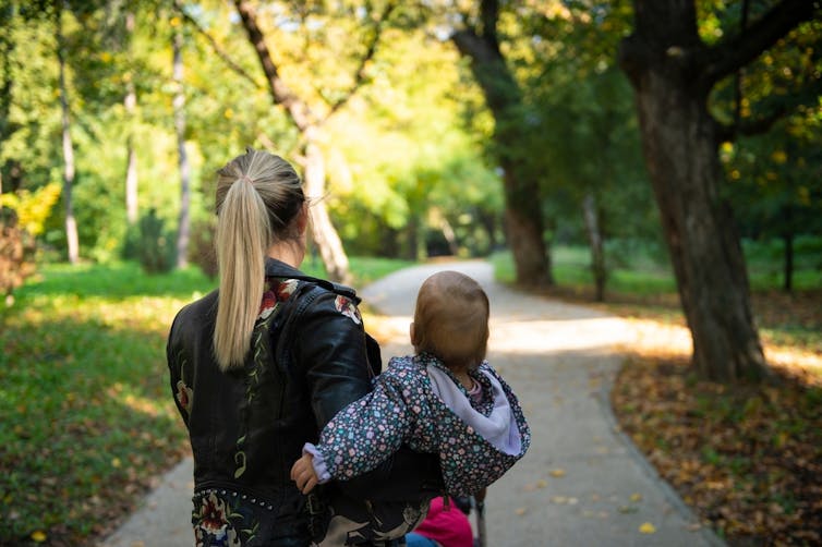 A woman holds her baby while walking in the park.