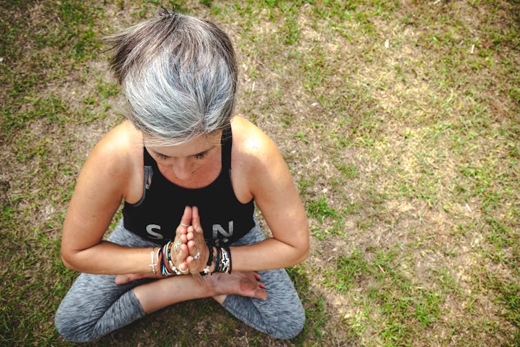 White haired woman doing yoga outside.