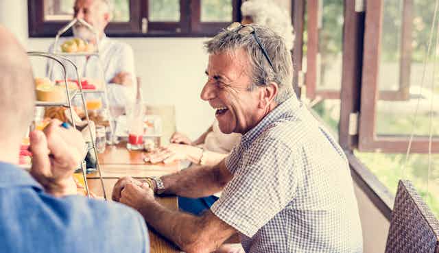 Older man laughs with friends at morning tea