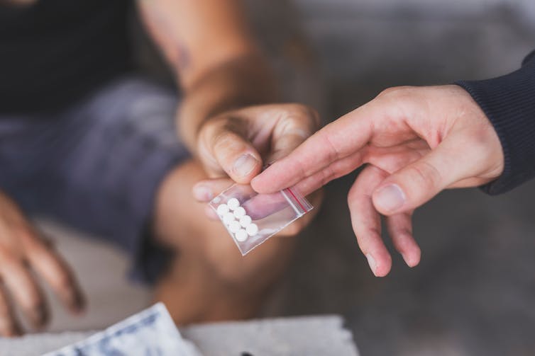 One person passing a small packet of pills to another person.