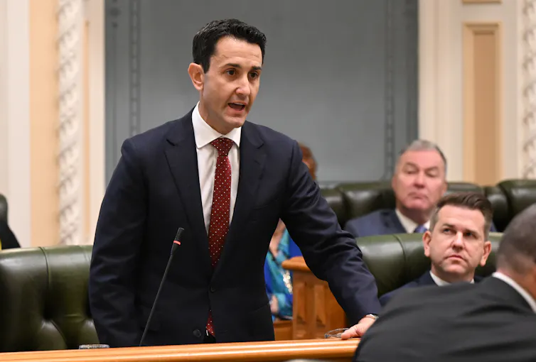 A man in a suit stands up and speaks into a microphone in parliament