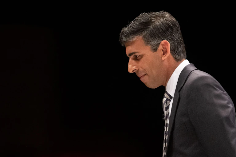RIshi Sunak in profile against a dark background.