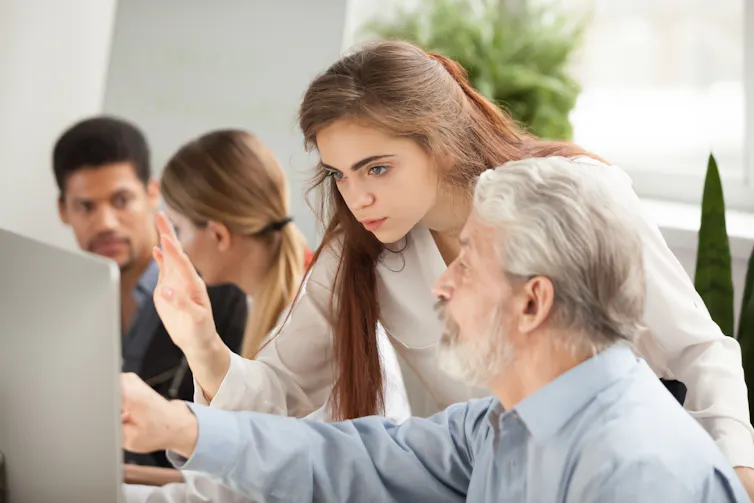 Une personne âgée posant une question à une jeune formatrice, l’enseignante l’aide à travailler sur ordinateur