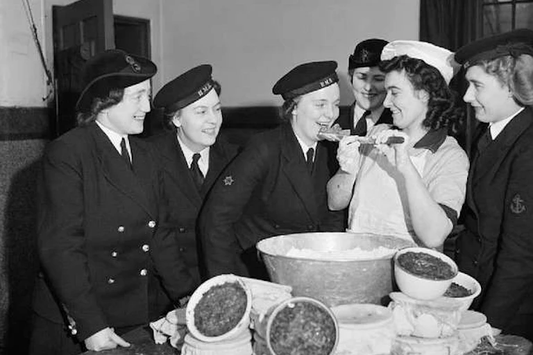 Vintage photo of smiling women in naval uniform with a woman in chef's uniform and bowls of Christmas pudding mix.