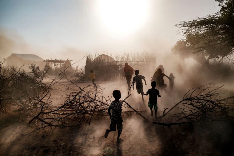 Silhouetted figures running in a cloud of dust