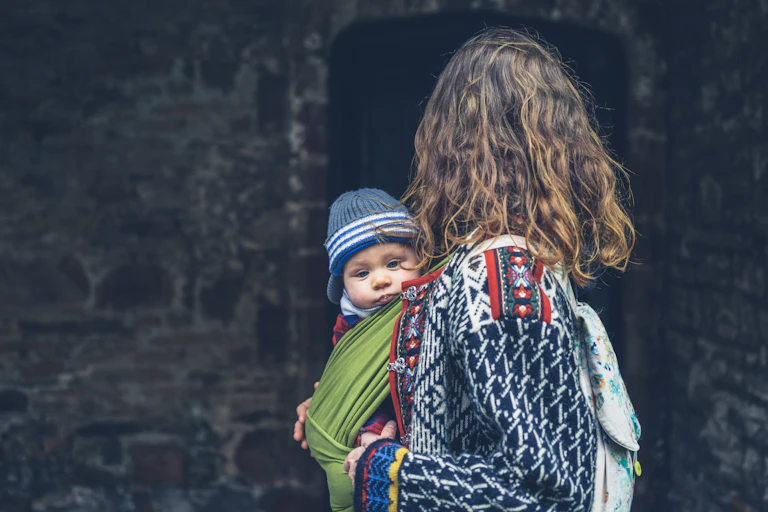 Une femme porte un enfant dans un porte-bébé placé sur le côté.