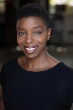An elegant African woman with natural hair and a black blouse smiles at the camera.