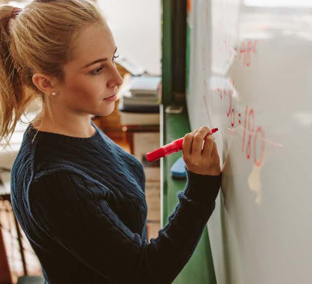 Young woman writing equation on whiteboard