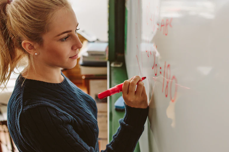 Young woman writing equation on whiteboard