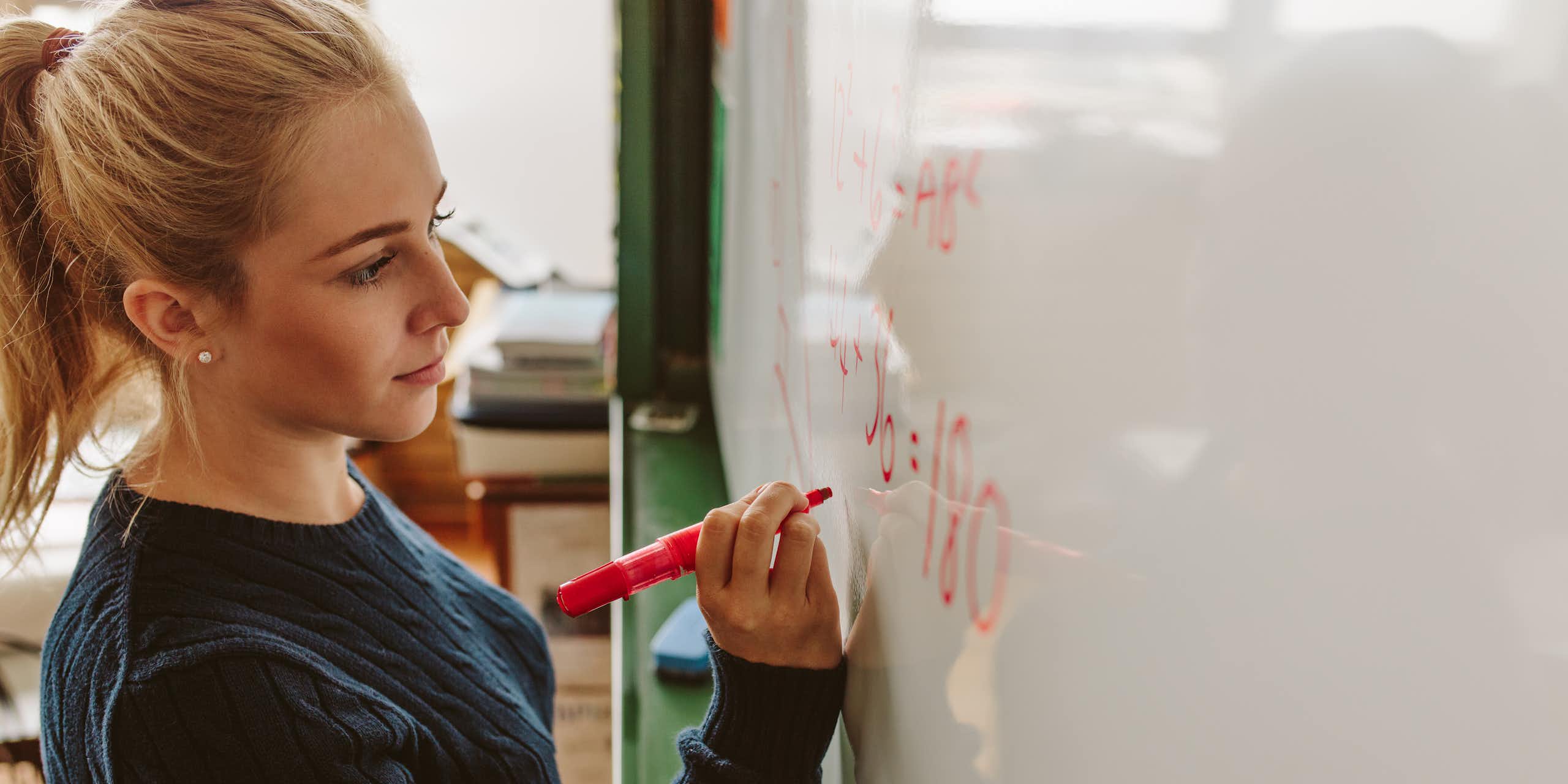 Young woman writing equation on whiteboard