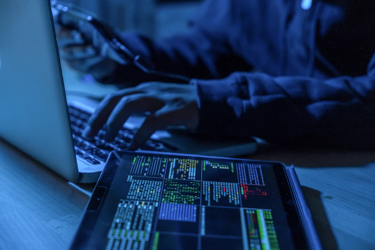 A man in a dark room is on a laptop, seemingly doing some shady stuff.