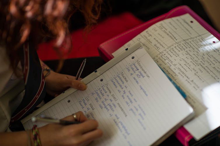 A close up of a person writing on an A4 paper pad.