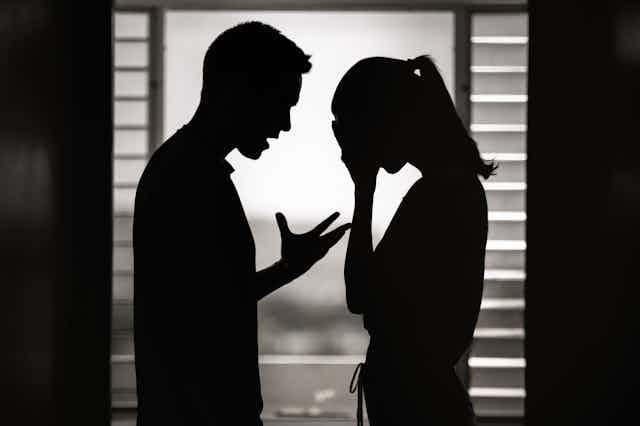 Silhouette of couple arguing in front of a window