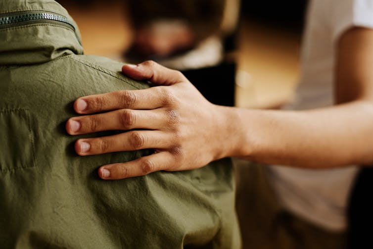 Close-up of person holding their hand on another person's shoulder in a supportive gesture