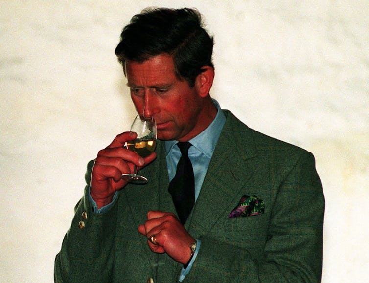 Flush young man wearing green suit jacket sniffs a glass of whiskey.