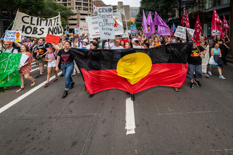 People marching with a large First Nations flag in the foreground