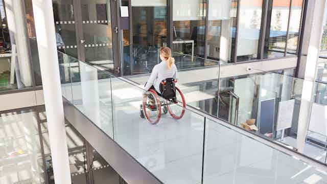 woman in wheelchairs crossing platform in office building