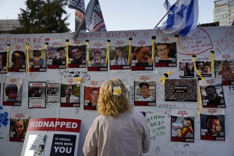 A woman is photographed from behind looking at a wall of photos of people abducted by Hamas militants. A sign beside her reads: 'Kidnapped: It could have been you.'