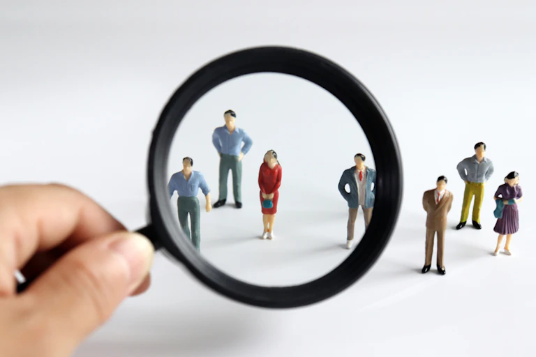 Homme cherchant une figurine de femme parmi des figurines d'hommes avec une loupe.