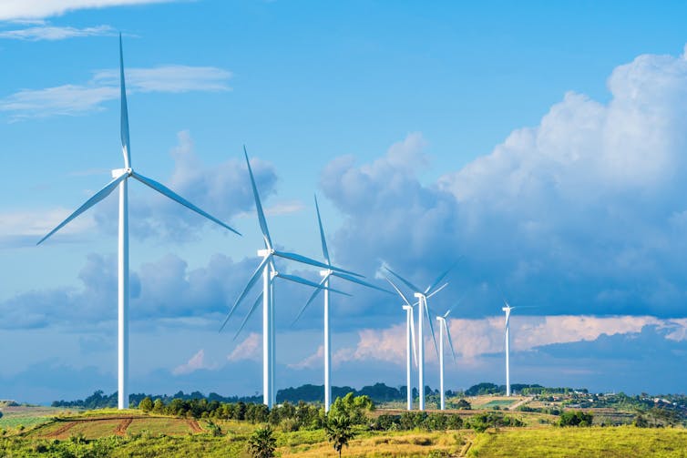 A wind farm on green fields against a cloudy sky.