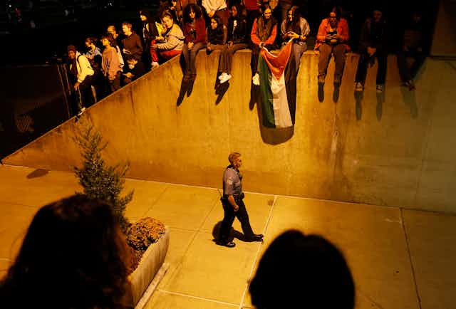 A police officer walks with students holding a Palestinian flag above him. 