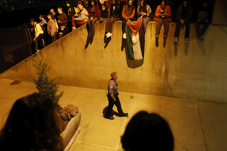 A police officer walks with students holding a Palestinian flag above him.