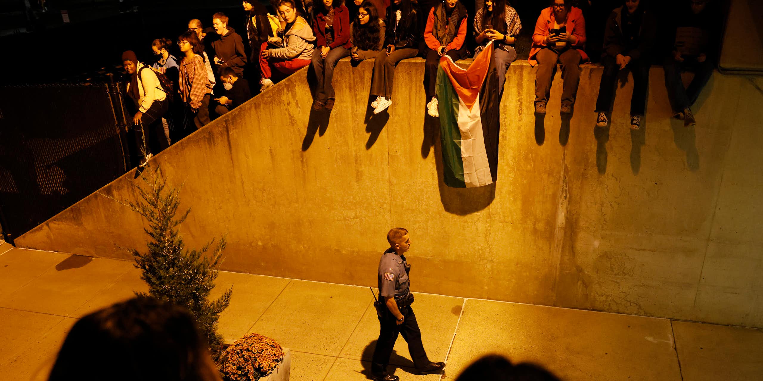 A police officer walks with students holding a Palestinian flag above him. 