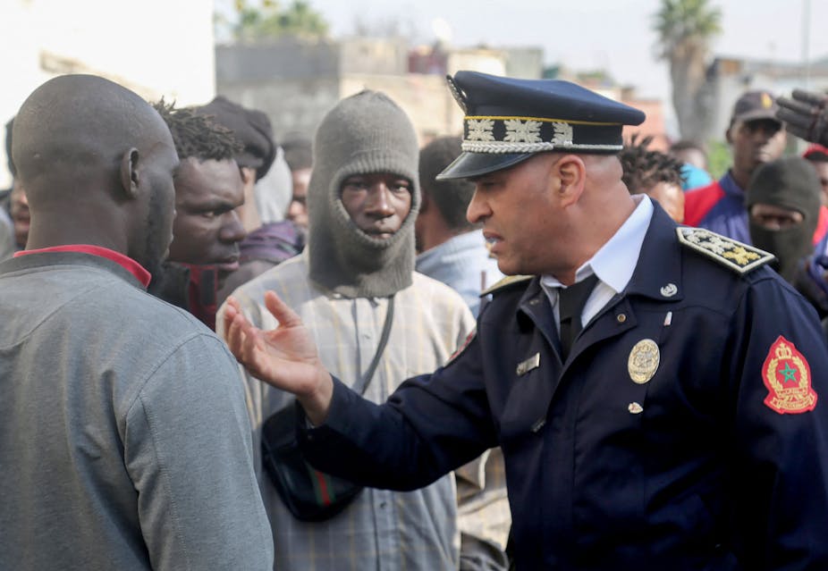Un policier marocain en uniforme discute avec des hommes noirs au milieu d'une foule
