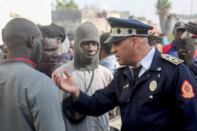 Un policier marocain en uniforme discute avec des hommes noirs au milieu d'une foule