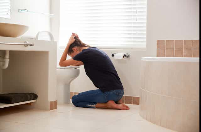 Woman with sickness bent over a toilet pan.