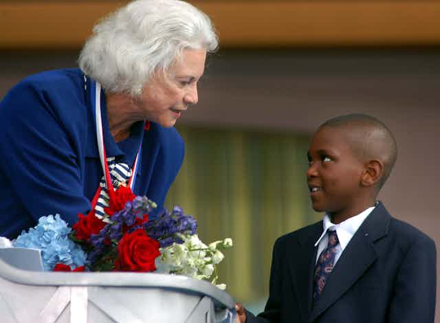 An older woman gets flowers from a young Black boy.