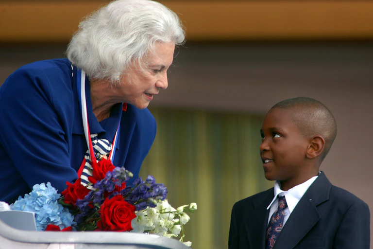 An older woman gets flowers from a young Black boy.