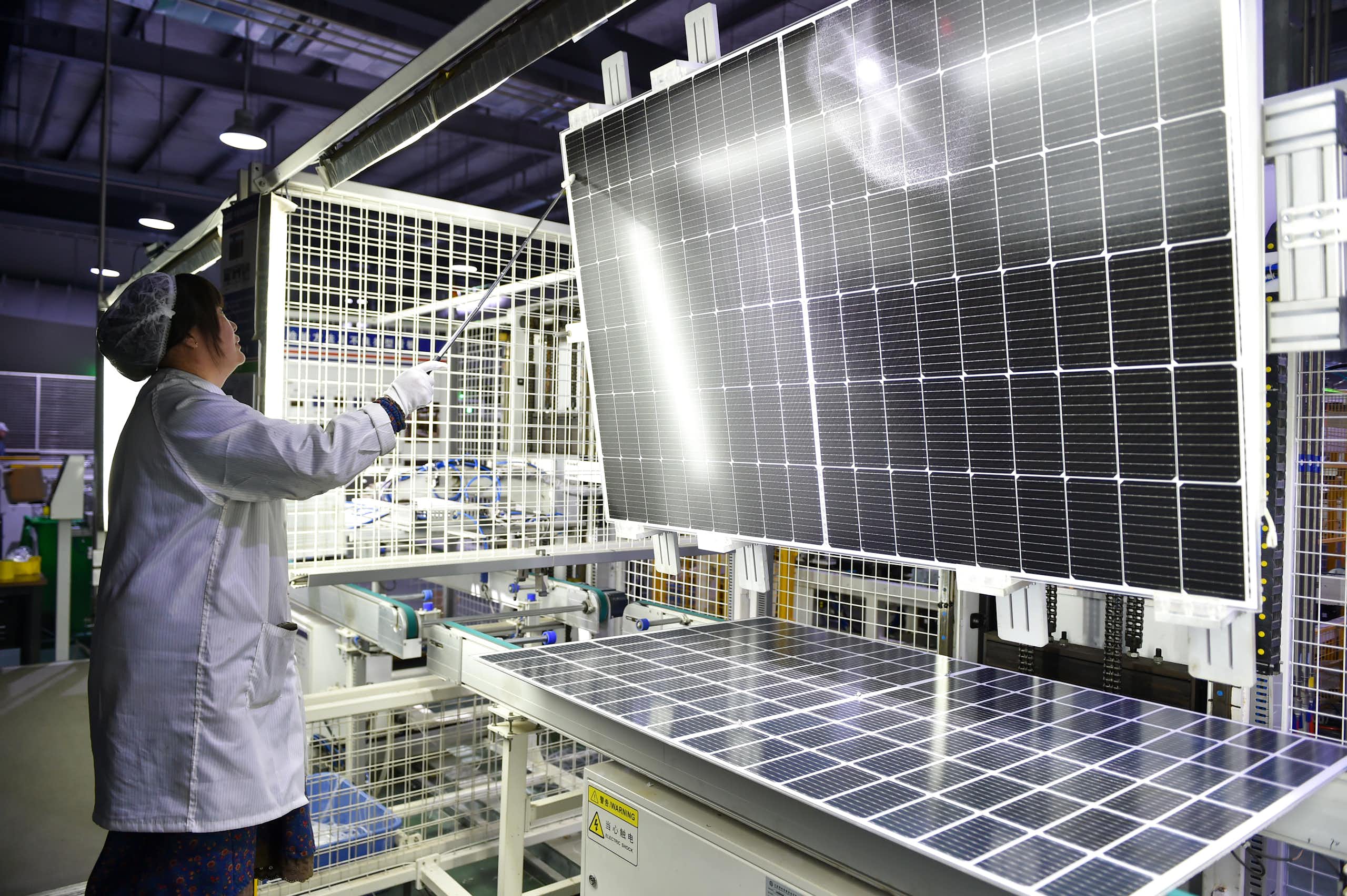 A woman worker wearing a white overall painstakingly assembles a solar energy panel in a high tech factory