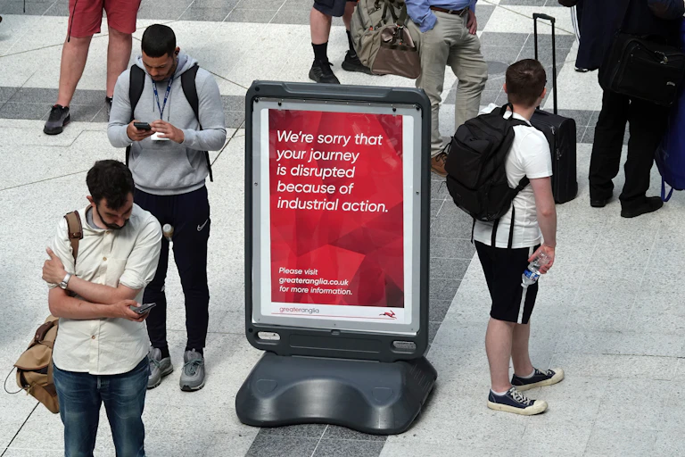 People standing around a sign at a station that apologises for disruptions because of industrial action.