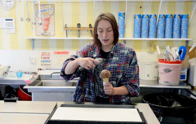 A teenager scoops ice cream in a shop.