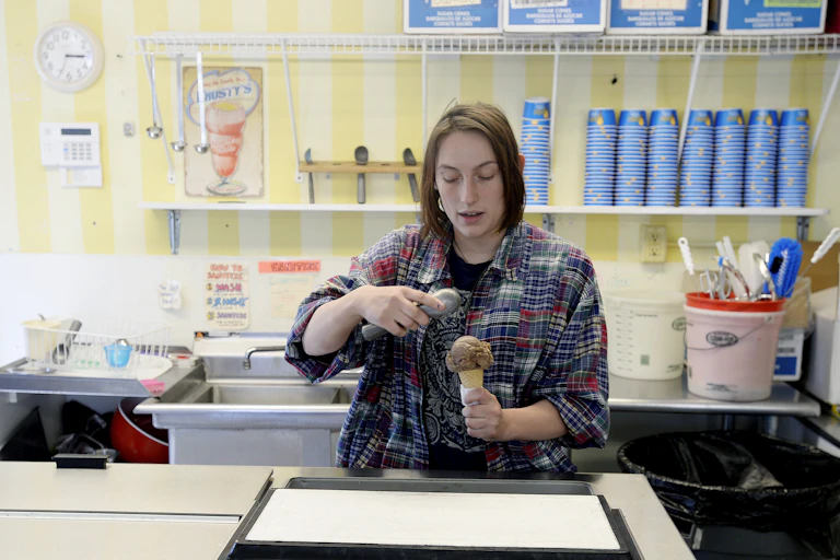 A teenager scoops ice cream in a shop.