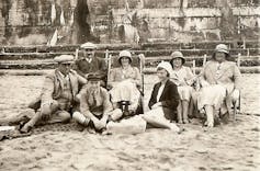 An archival photograph of people on deckchairs on a beach.