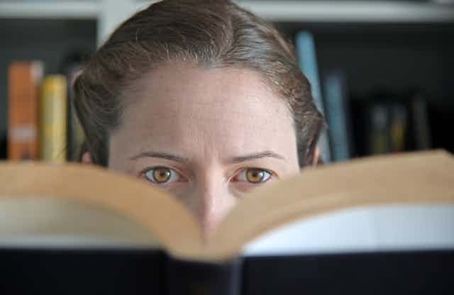 The top half of a woman's face seen behind a book.