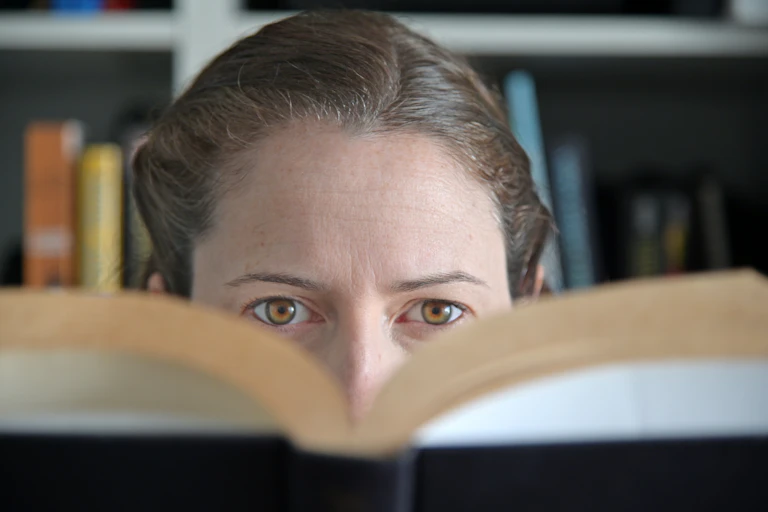 The top half of a woman's face seen behind a book.