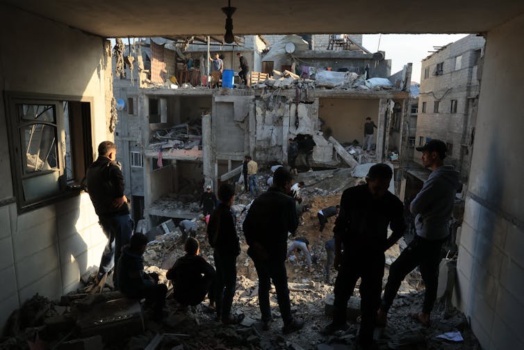 A group of men are standing near buildings that have been destroyed and reduced to rubble.