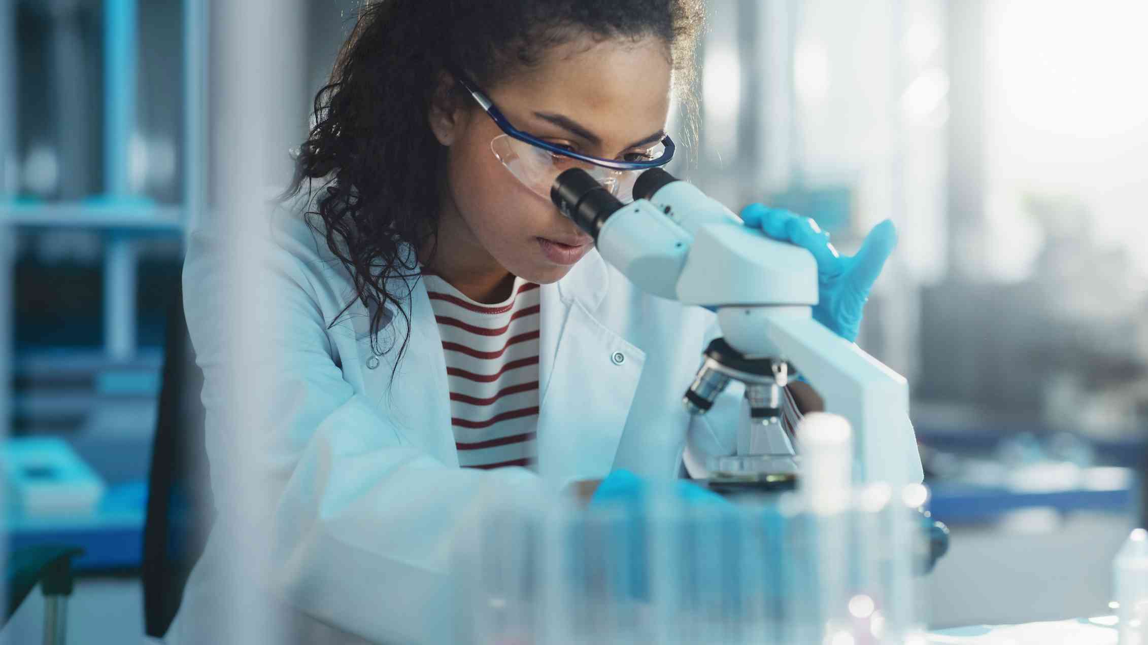 A black woman in a lab coat looking through a microscope